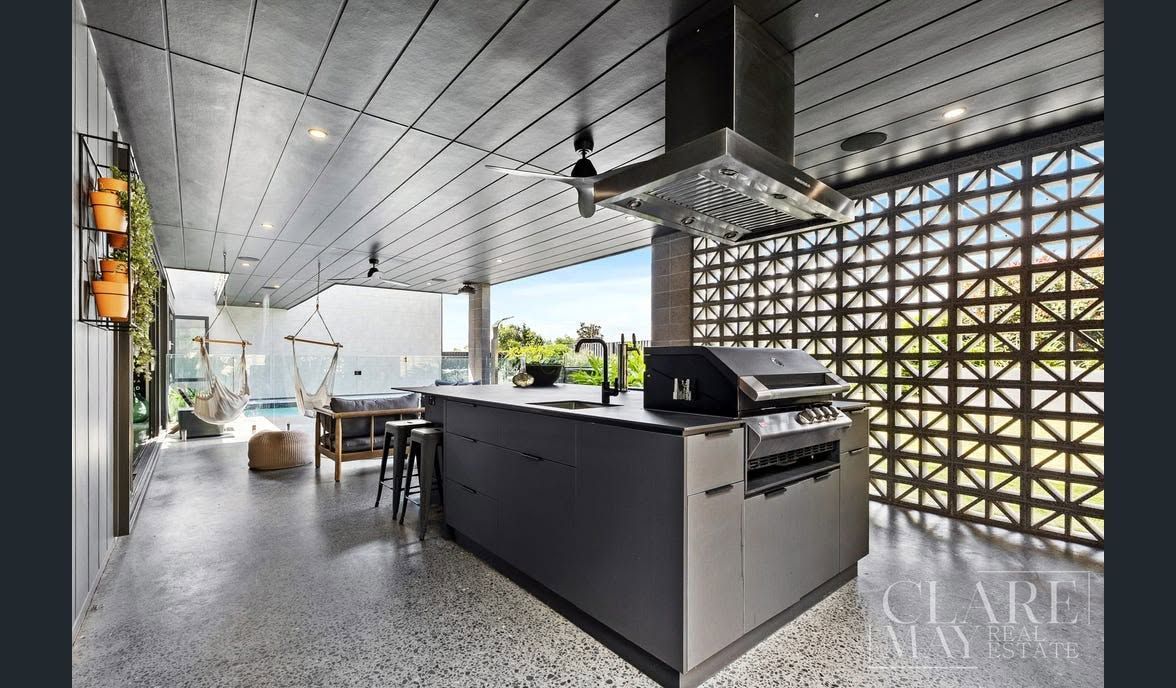 Modern outdoor kitchen with grill island, dining table, and patterned concrete block wall under a covered patio