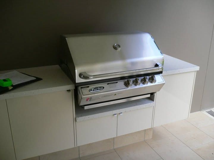 Stainless steel gas grill built into a white outdoor countertop on a tiled patio.