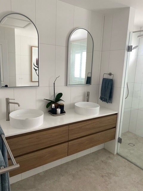 Modern bathroom with double vanity, round mirrors, white sinks, and light wood cabinets.