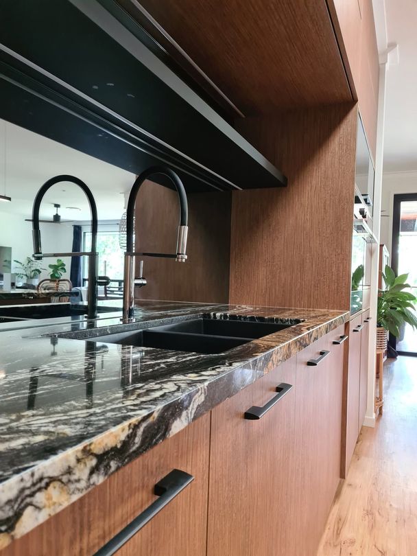 Modern kitchen counter with black marble, wood cabinets, and double black faucets by a bright window Modern kitchen counter with black marble, wood cabinets, and double black faucets by a bright window