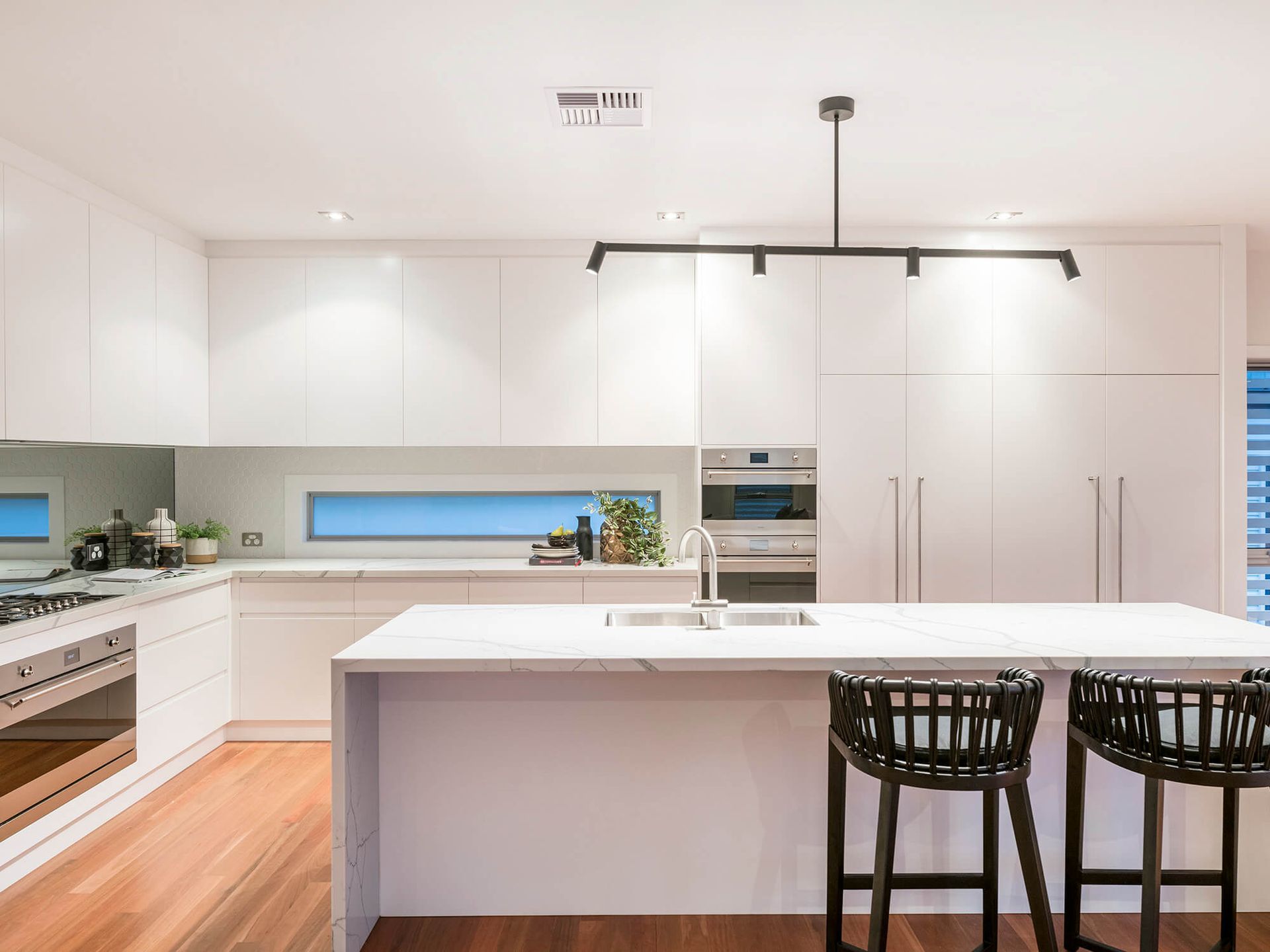 Modern white kitchen with island, black bar stools, and wood flooring Modern white kitchen with island, black bar stools, and wood flooring