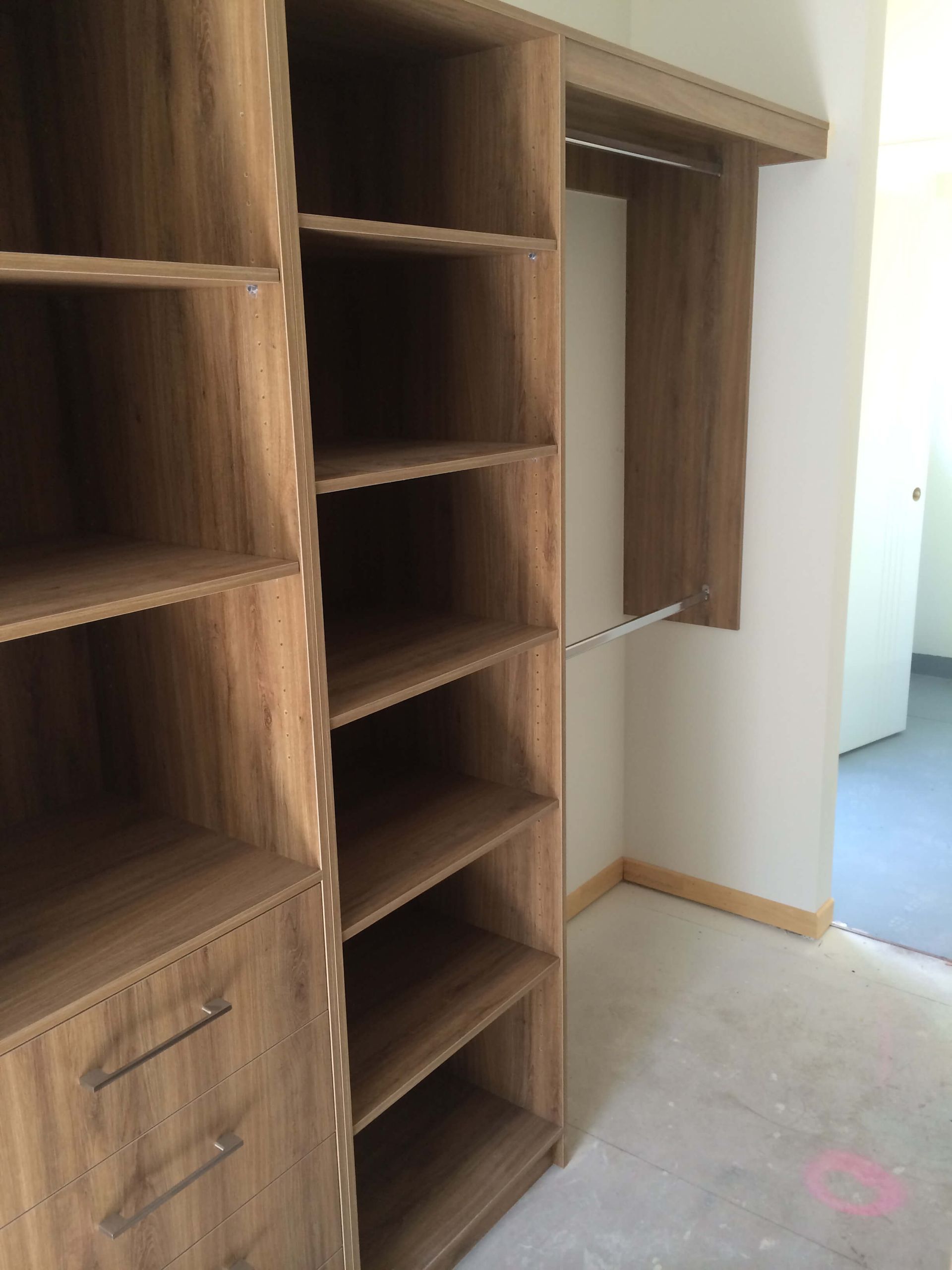 Built-in wooden closet shelves and hanging rod in an empty room with carpeted floor.