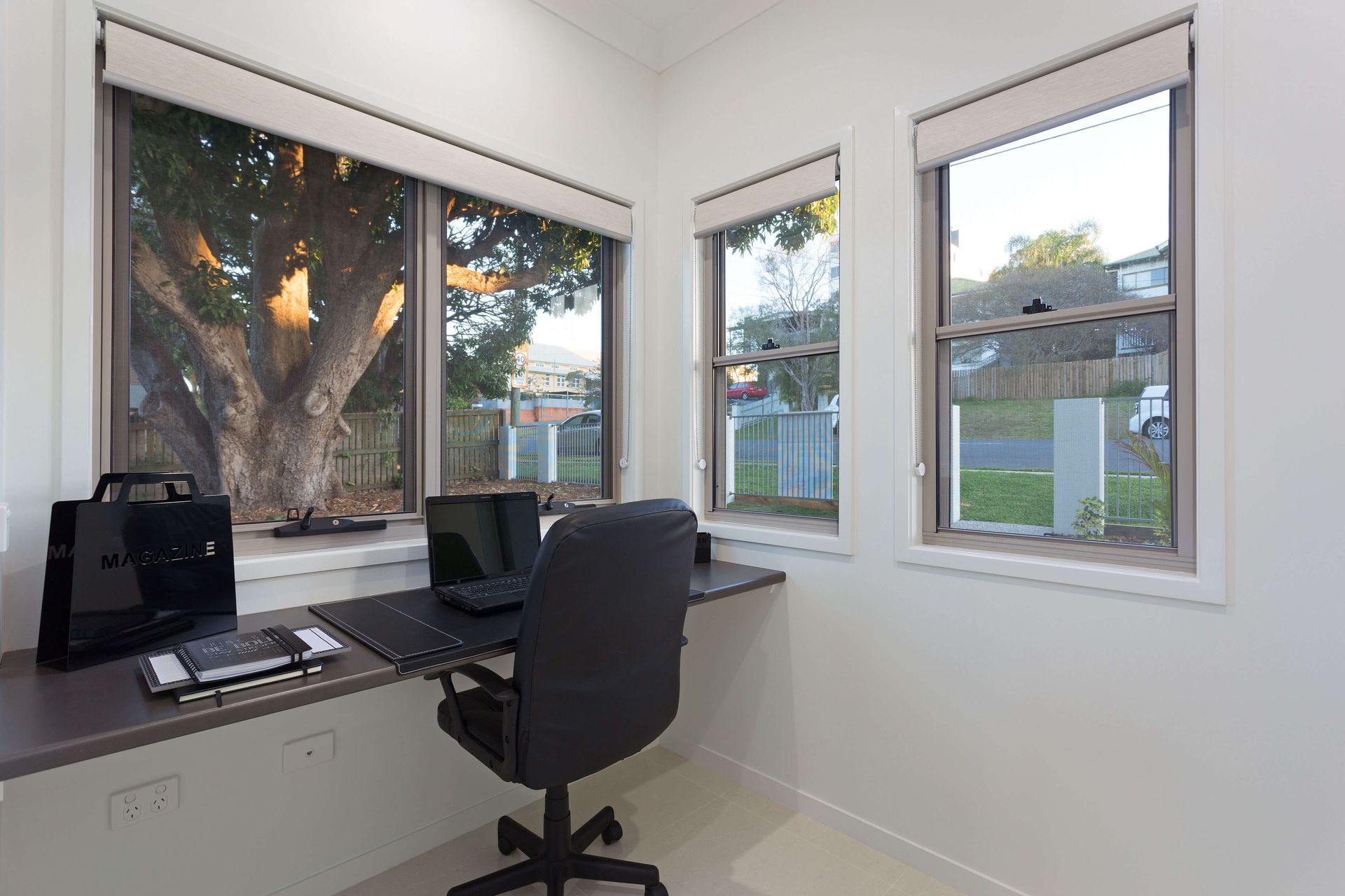 Small home office with desk, laptop, chair, and three windows overlooking a yard