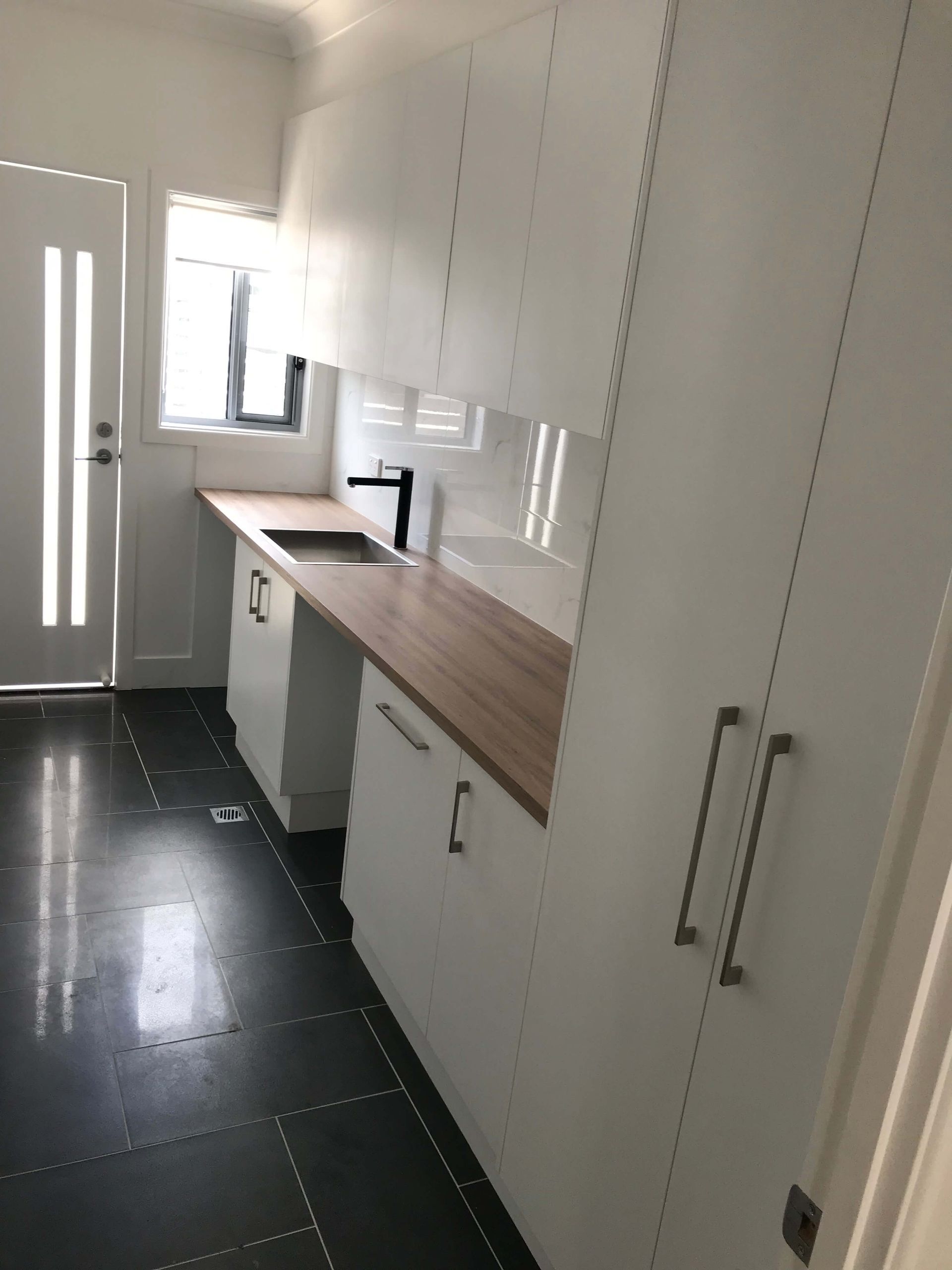 Modern white kitchen with wood countertops, black tiled floor, and a bright window near the sink