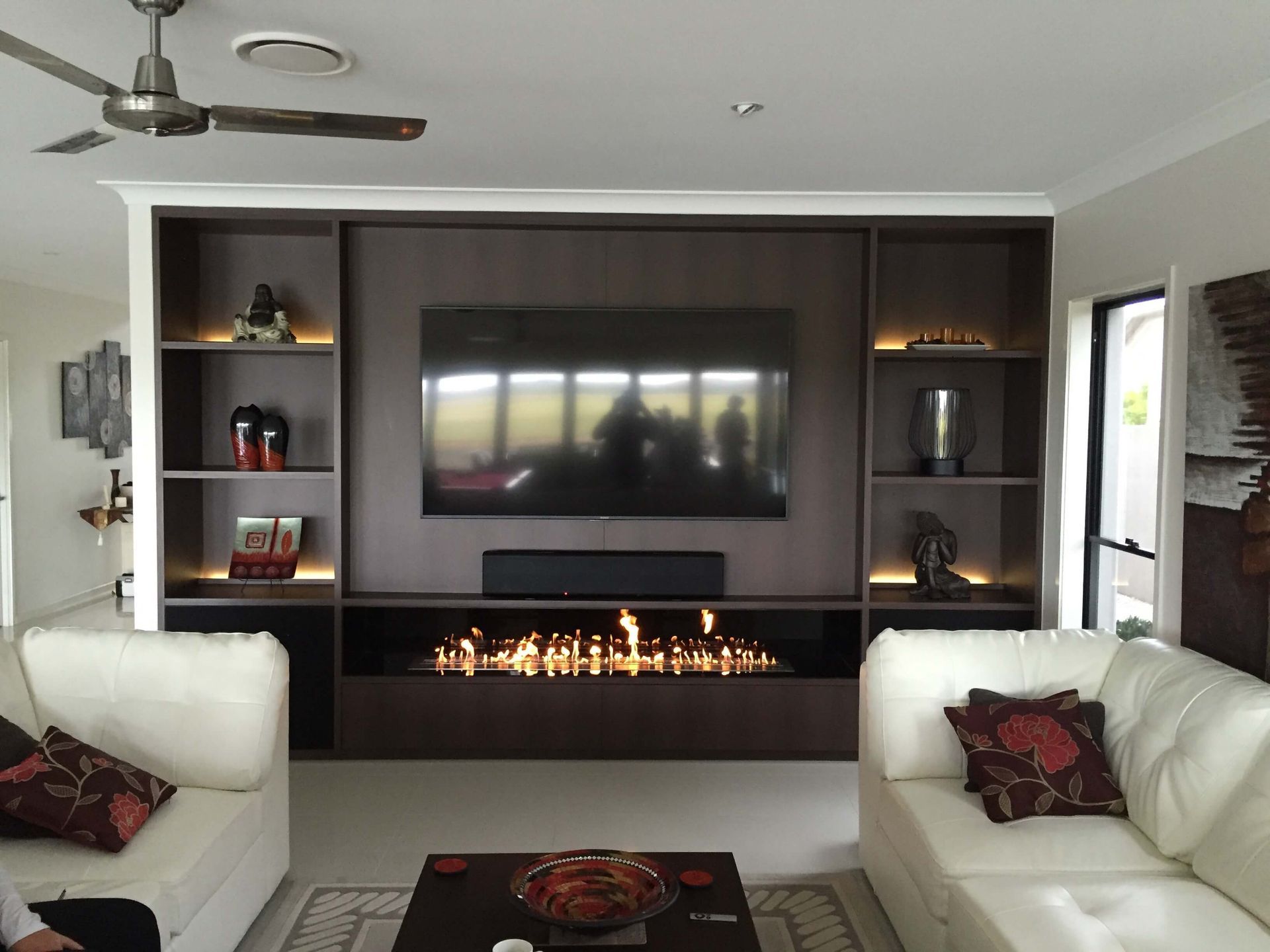 Modern living room with wall-mounted TV, electric fireplace, and white sofas