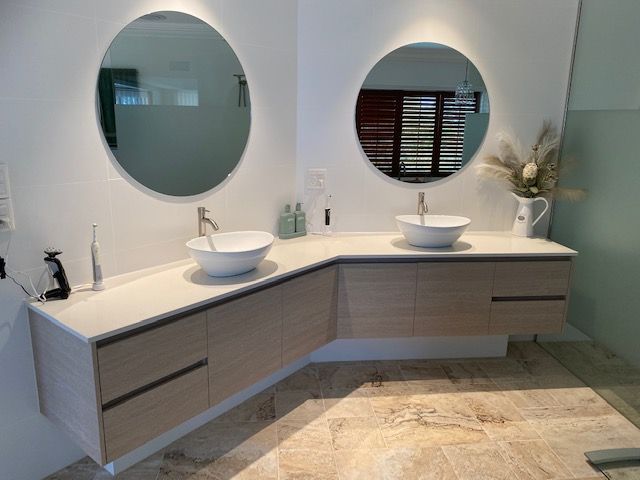 Modern bathroom with double round mirrors, white sinks, and light wood vanity under curved countertop