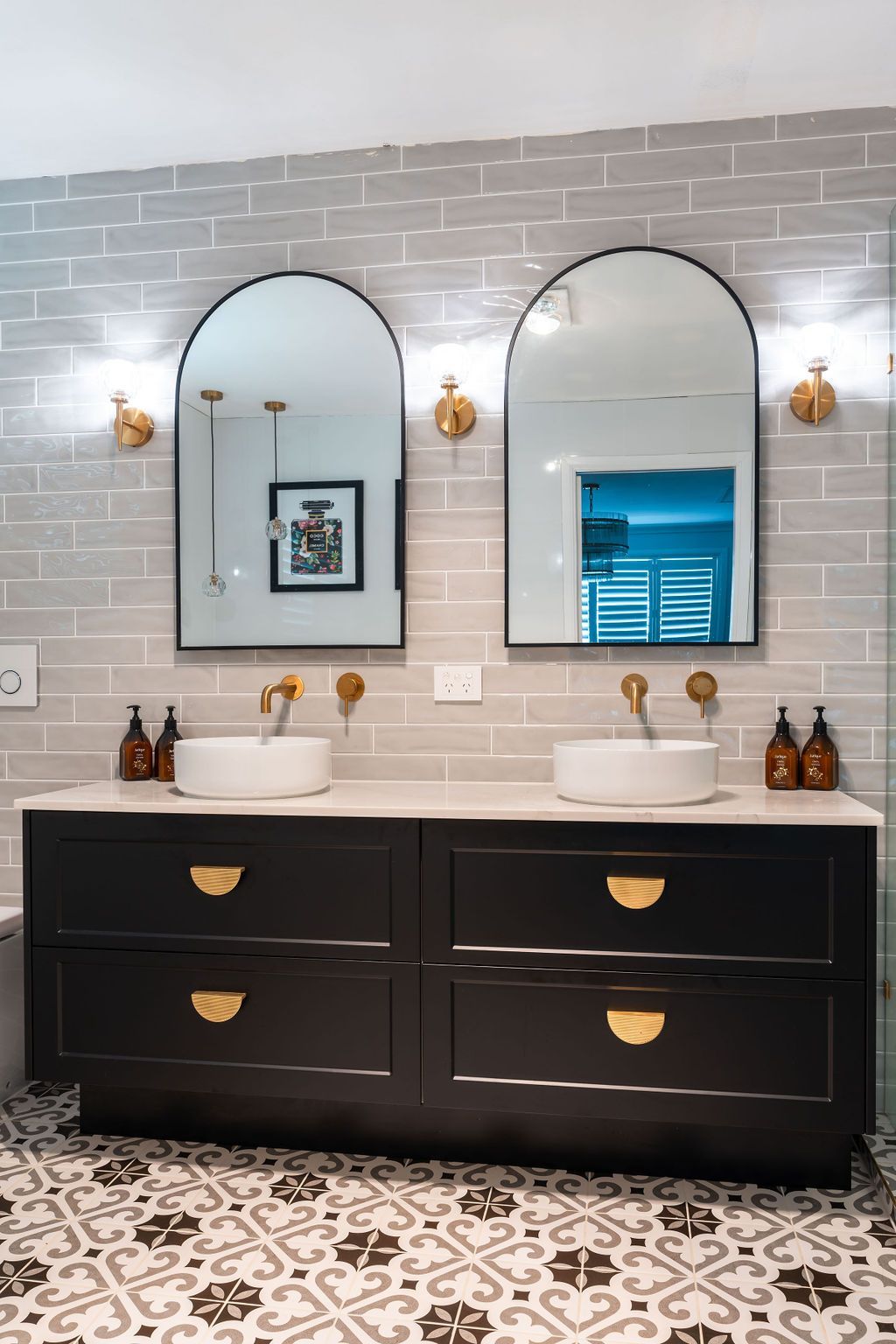 Modern double vanity bathroom with black cabinets, arched mirrors, and patterned tile floor