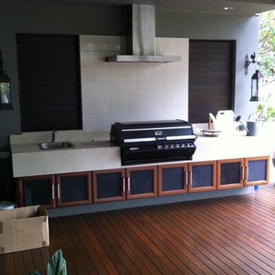 Outdoor kitchen with built-in grill, white countertop, and wooden cabinet doors on a deck