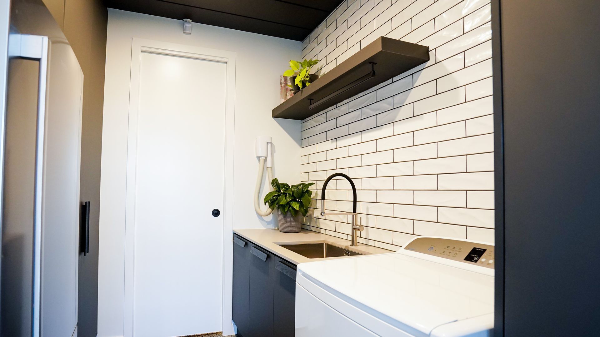 Modern kitchen nook with white cabinets, black countertop, sink, floating shelf, and brick-pattern backsplash