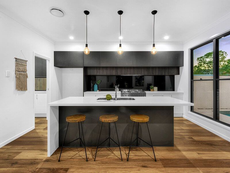 Modern kitchen with white island, dark cabinets, three bar stools, and large windows overlooking greenery Modern kitchen with white island, dark cabinets, three bar stools, and large windows overlooking greenery