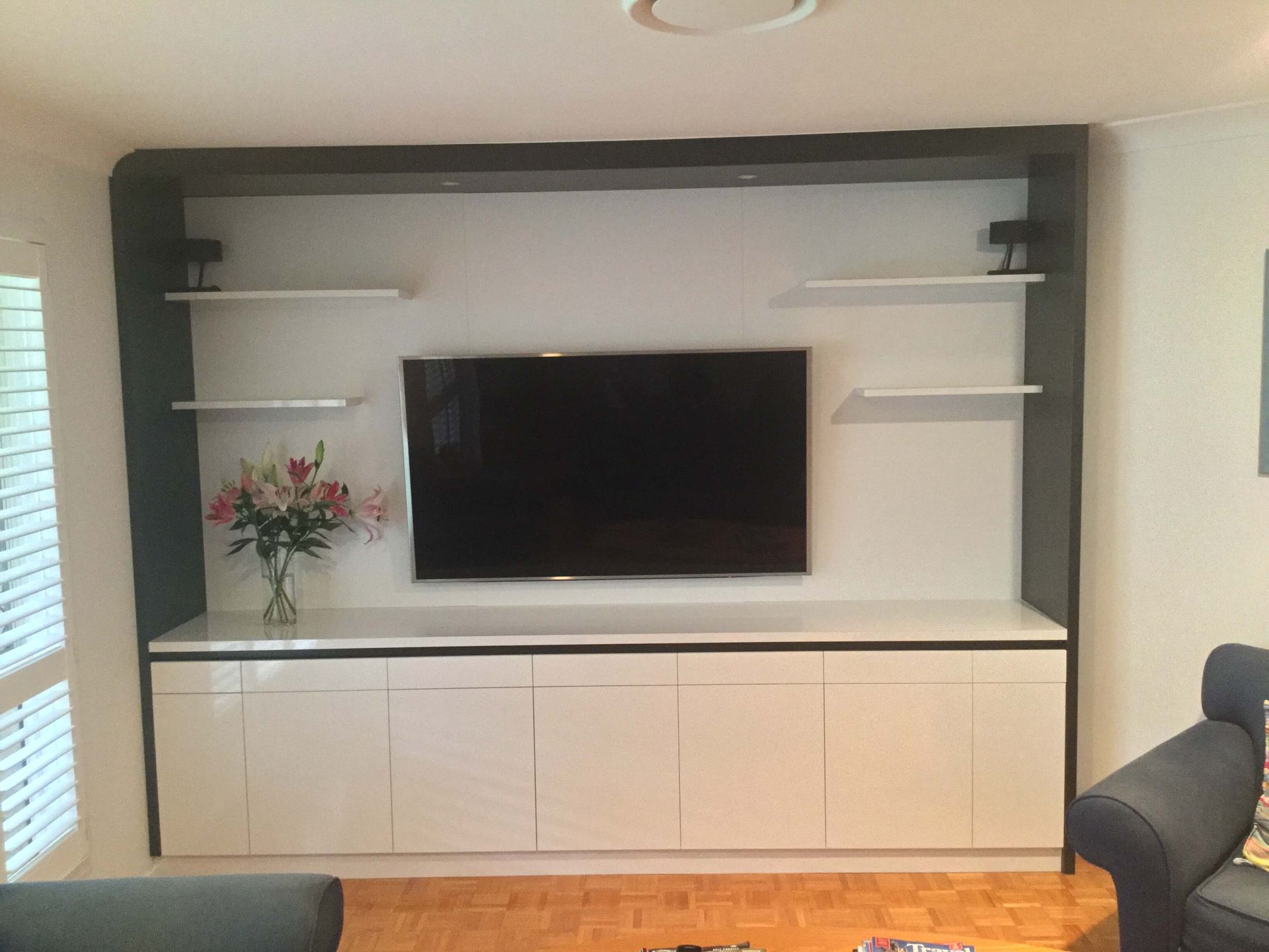 Modern living room wall unit with TV, white cabinets, black shelves, and a flower vase