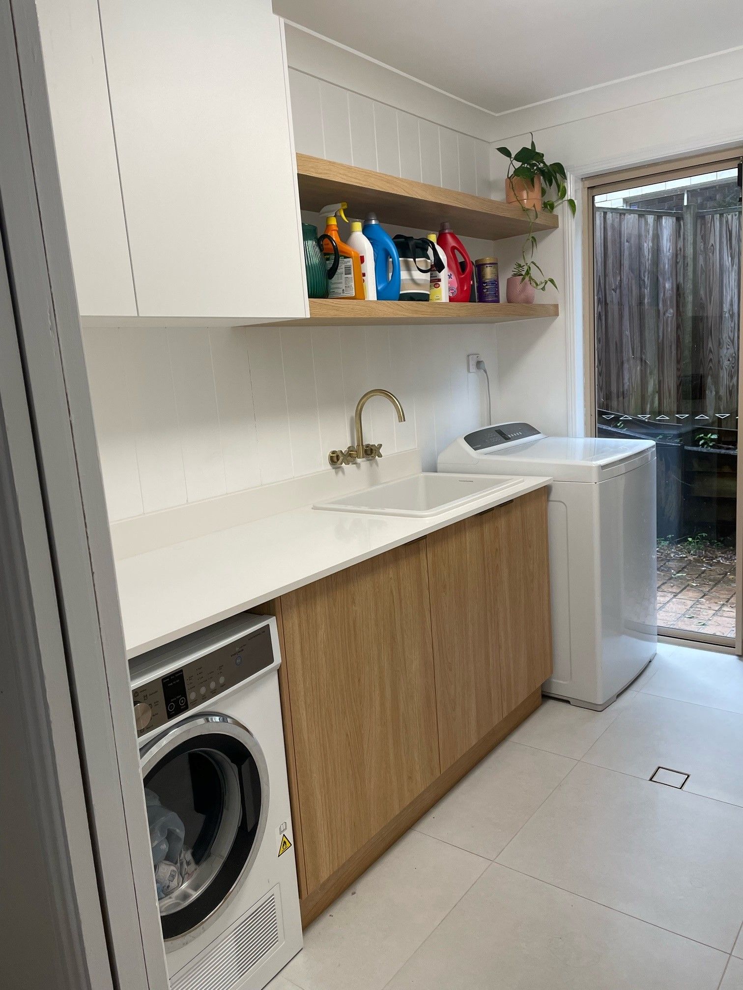 Modern laundry room with white cabinets, wood countertop, sink, washing machine, and a view to a balcony.