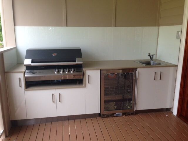 Outdoor kitchen with built-in grill, white cabinets, wine cooler, and sink under a covered patio