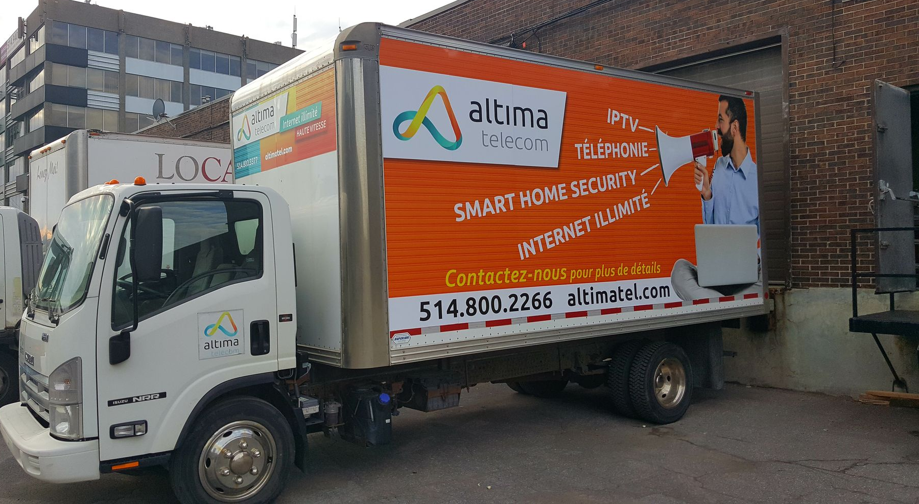 White truck with a colorful ad for Aluma Telecom parked by a brick building.