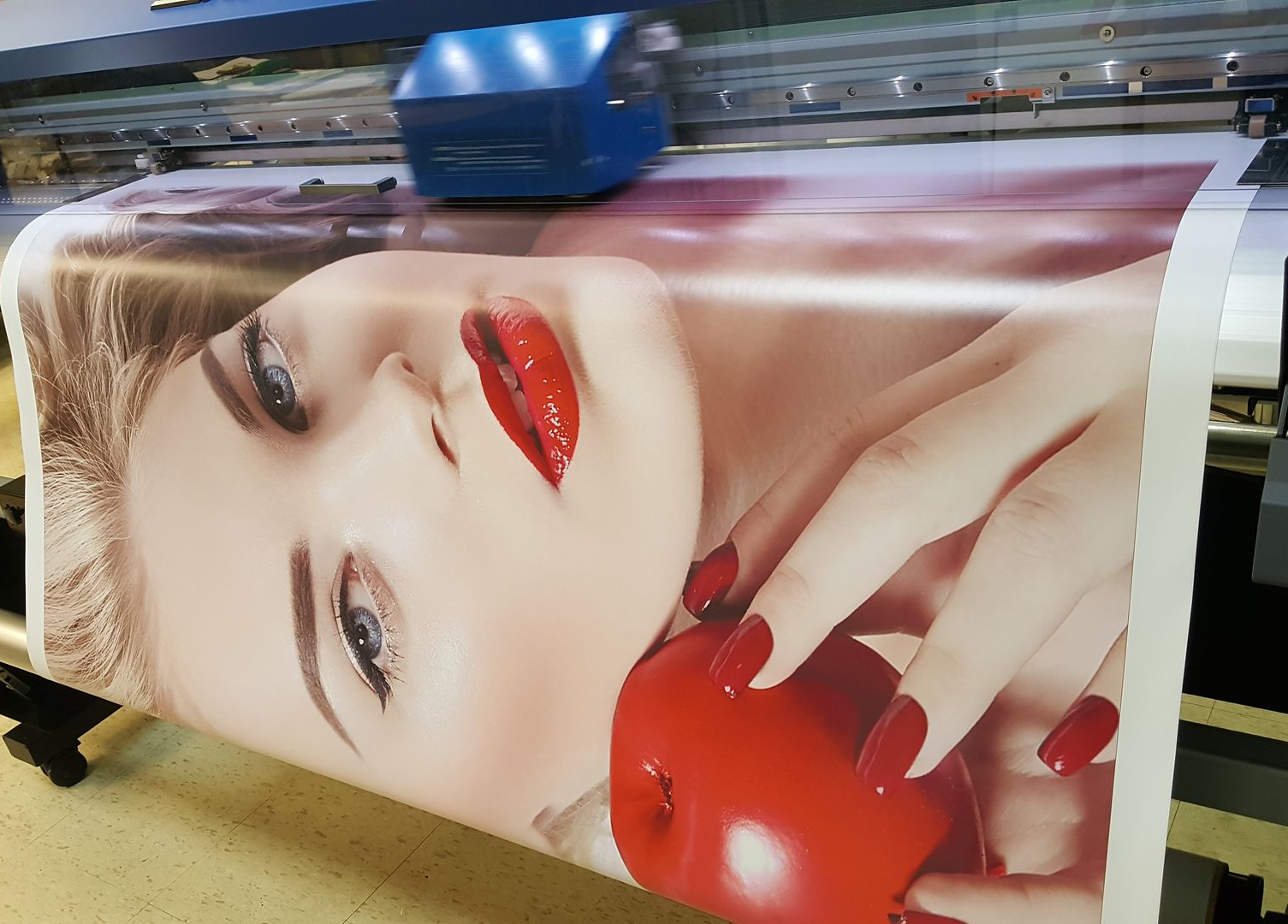 Large format printer printing a close-up of a woman's face with red lipstick and an apple.