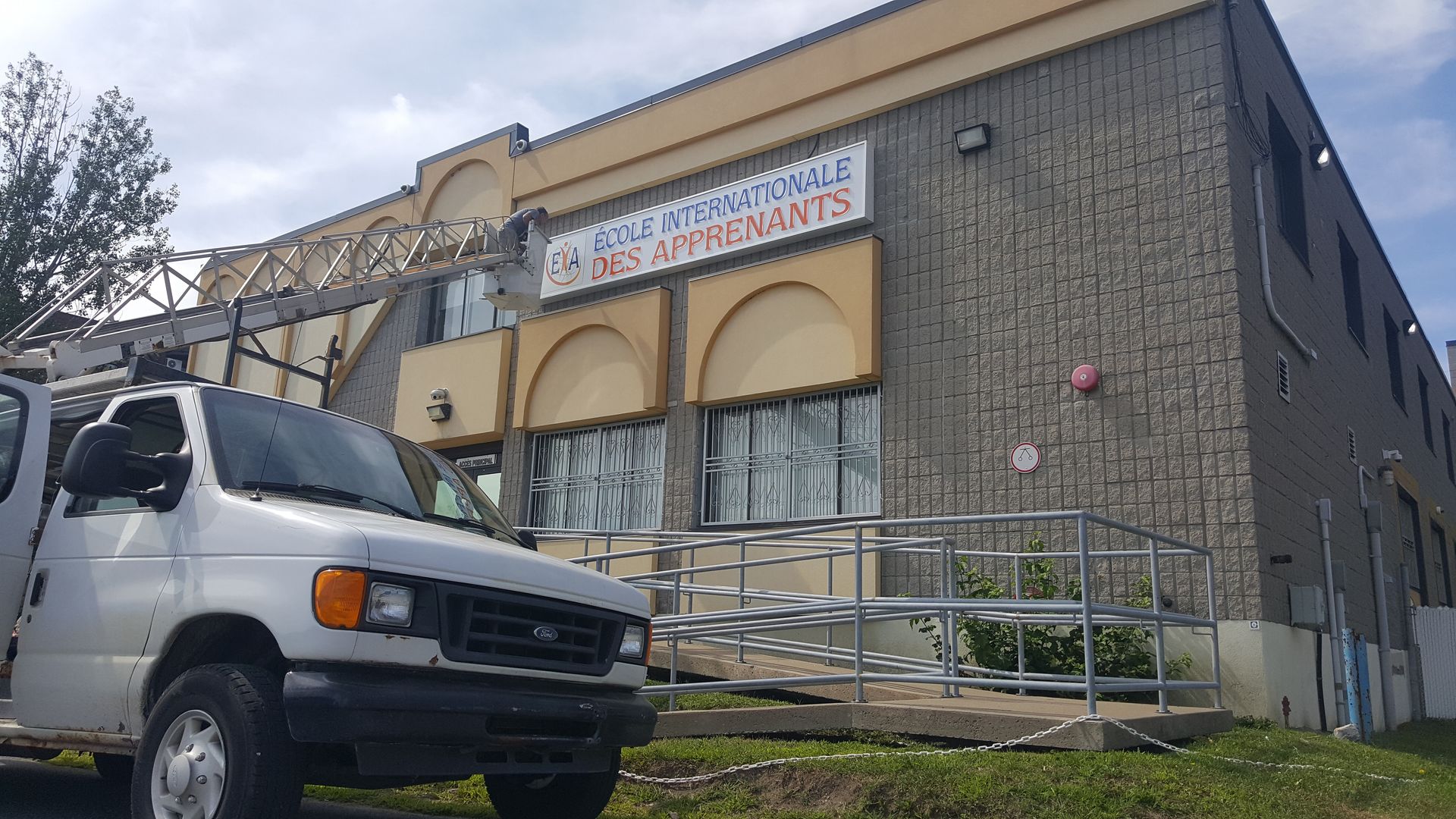 White van parked in front of a two-story building with a ramp and a sign reading