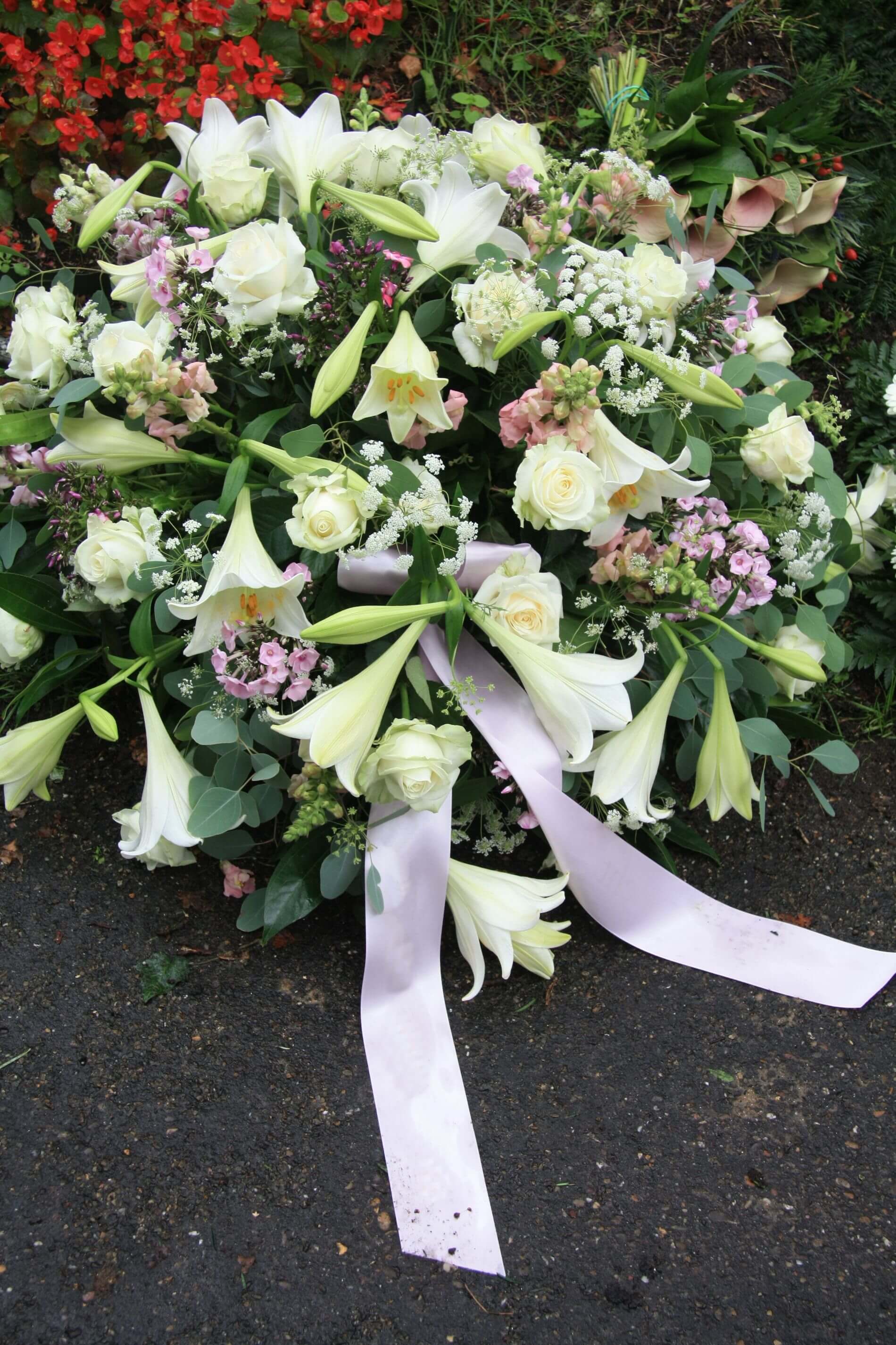 Un grande mazzo di fiori bianchi con un nastro rosa a terra.