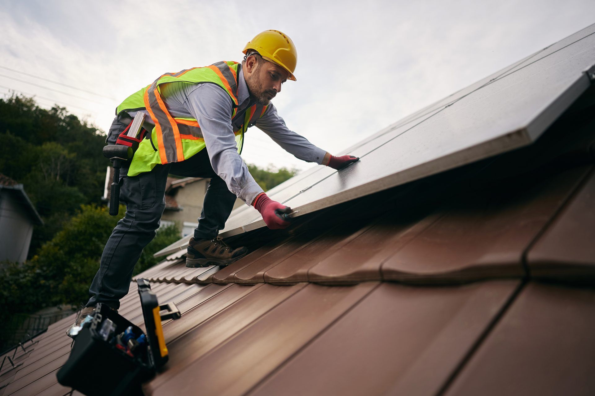 Roofer in safety gear laying shingles on a sloped roof
