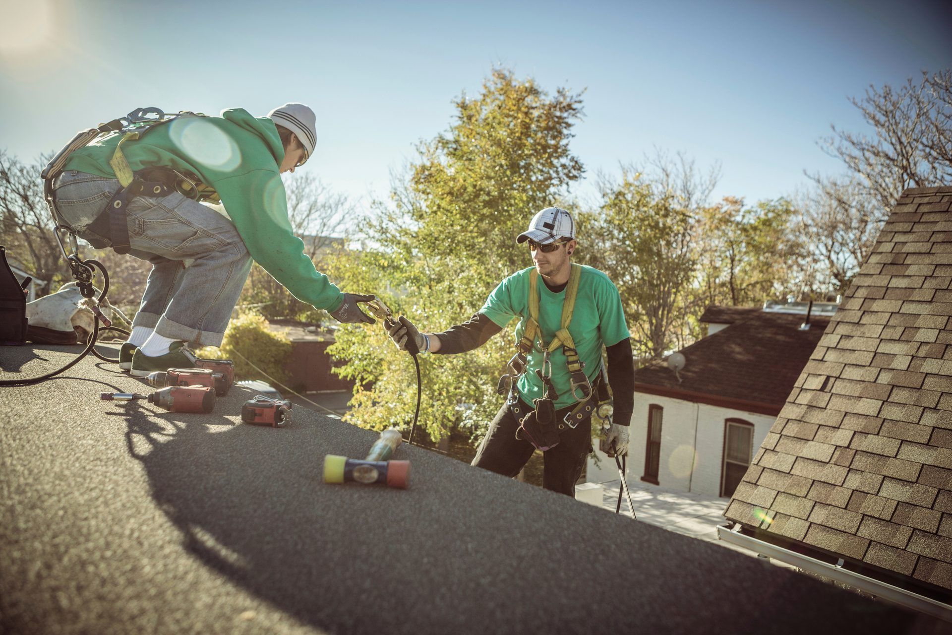 Roofers working on a shingle roof of a home surrounded by trees