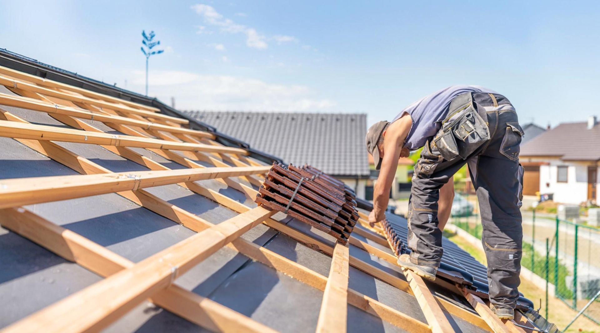 Roofer bending over a roof deck laying rows of new roofing tiles on timber battens