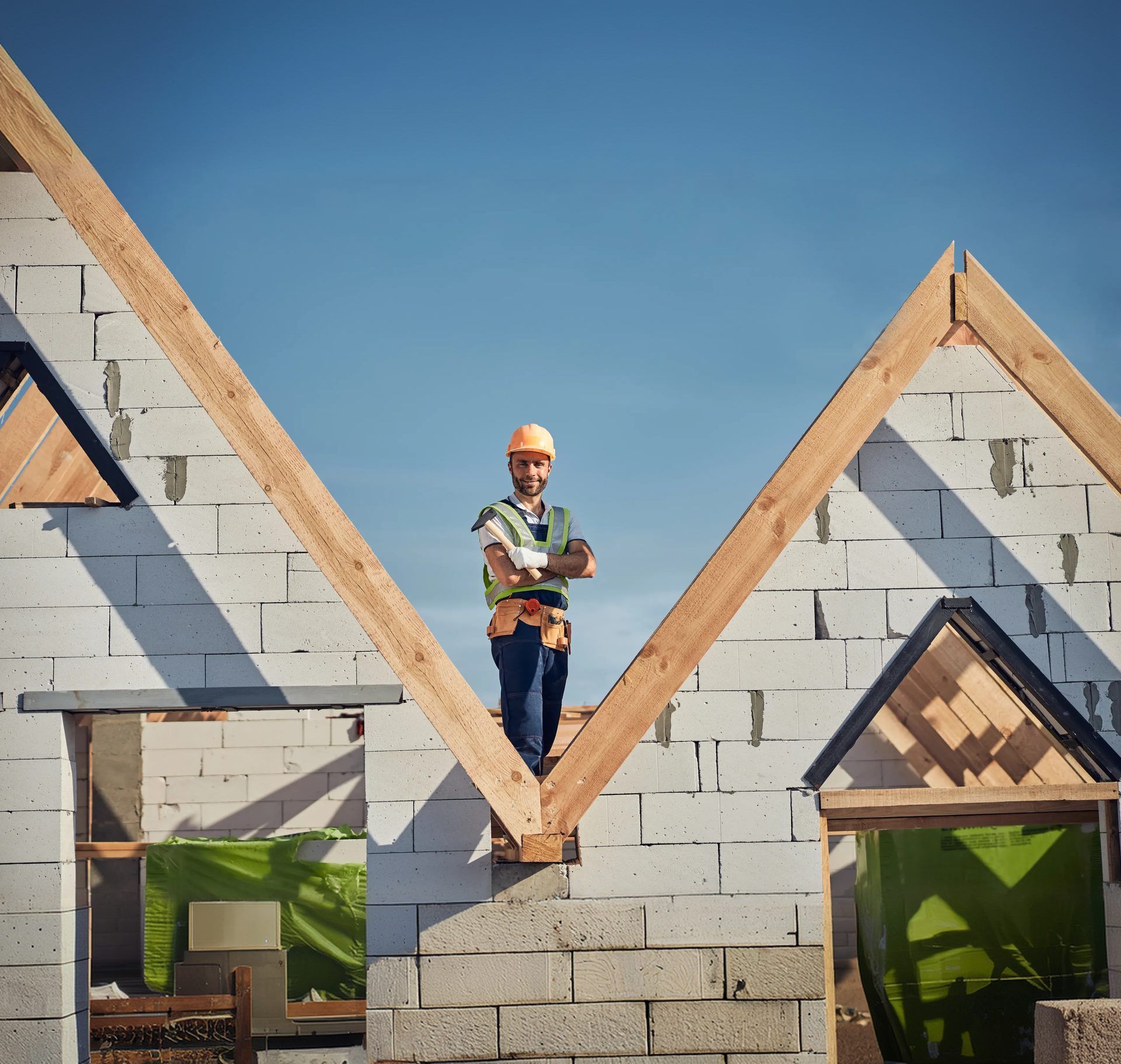 Construction worker standing between the exposed timber roof trusses of a part-built block home