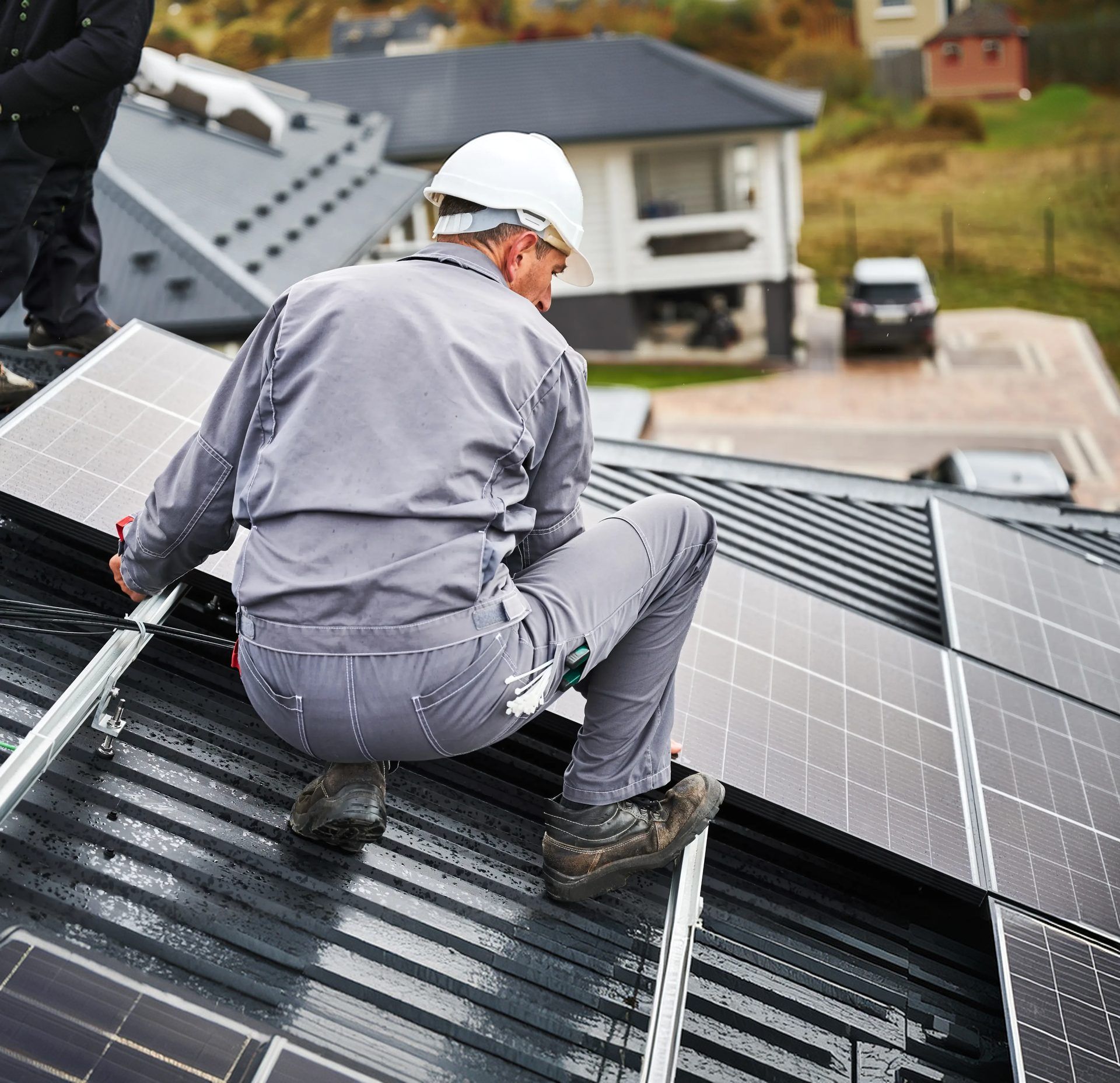 Roofer securing mounting rails across a metal roof on a hillside home