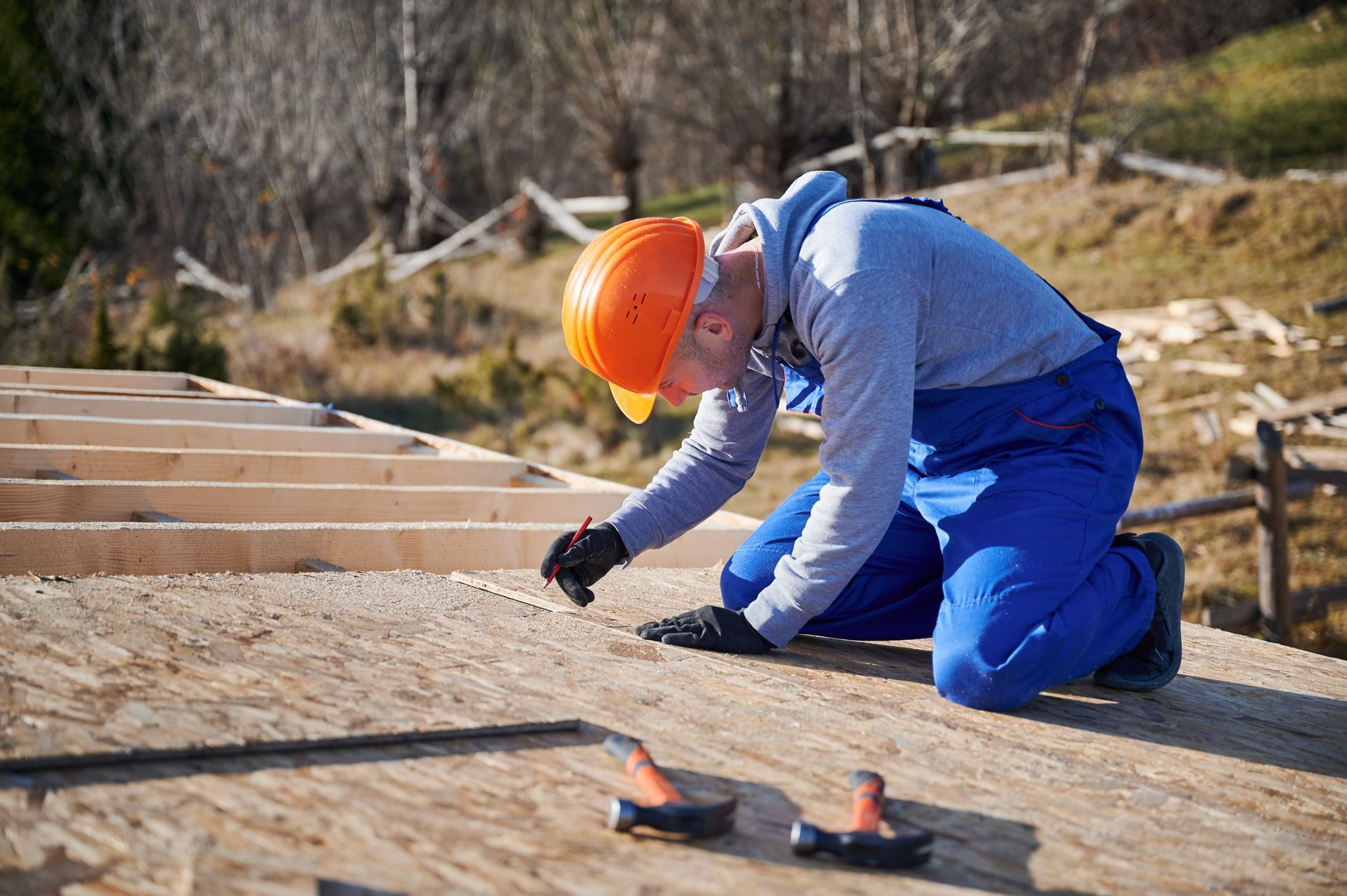 Roofer in an orange hard hat marking plywood roof sheathing with a pencil