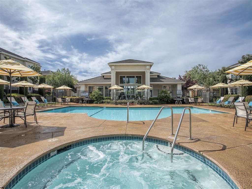 Outdoor community pool area with lounge chairs, umbrellas, and a clubhouse in the background at Iron Point at Prairie Oaks apartments in Folsom, CA.
