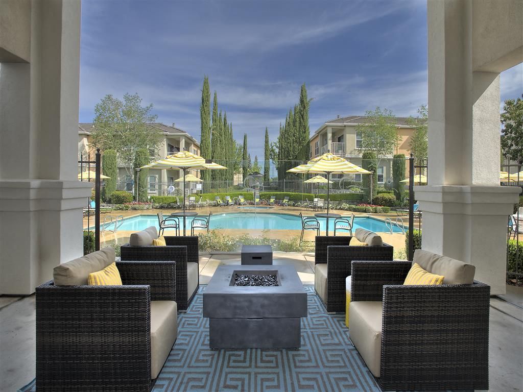 Outdoor community pool area with lounge seating under a covered patio and yellow umbrellas at Iron Point at Prairie Oaks apartments in Folsom, CA.