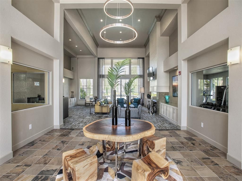Modern multifamily lobby with a round wooden table centerpiece and lounge seating at Iron Point at Prairie Oaks apartments in Folsom, CA.