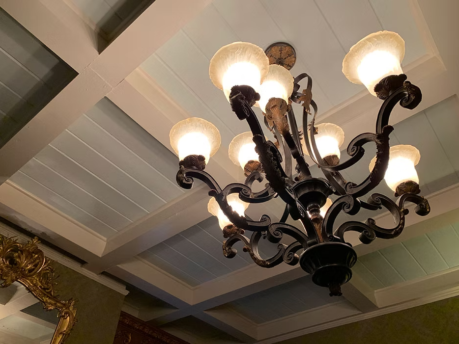 A dark, ornate chandelier with lit frosted-glass shades hangs from a white, coffered ceiling.