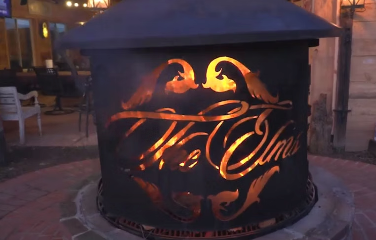 A glowing metal fire pit at night with the words