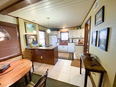 A rustic kitchen with wood cabinets, white appliances, a small island, and a dining table in the foreground.