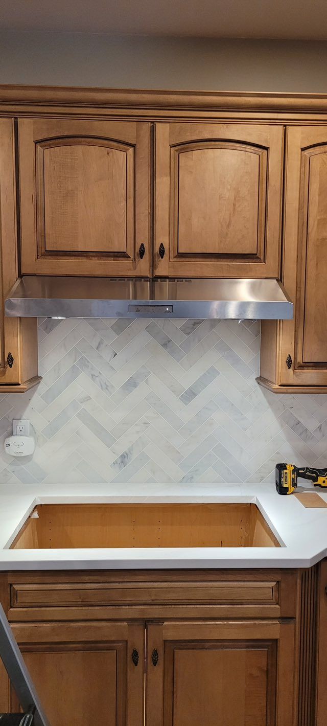 Kitchen with wooden cabinets, a stainless steel range hood, and a herringbone tile backsplash.