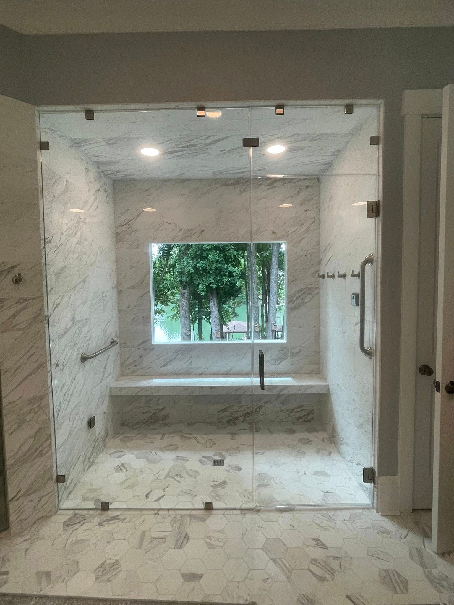 Glass-enclosed shower with marble tile walls, a window, and a built-in bench.