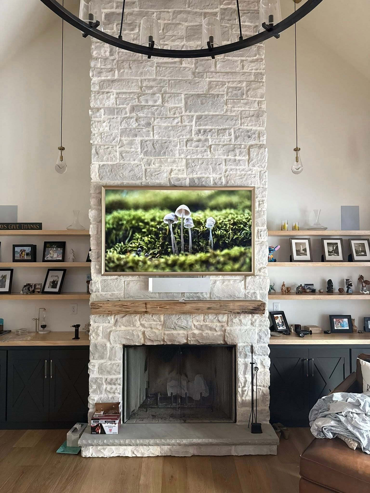 Stone fireplace with built-in shelves and a mounted TV. A black chandelier hangs above.