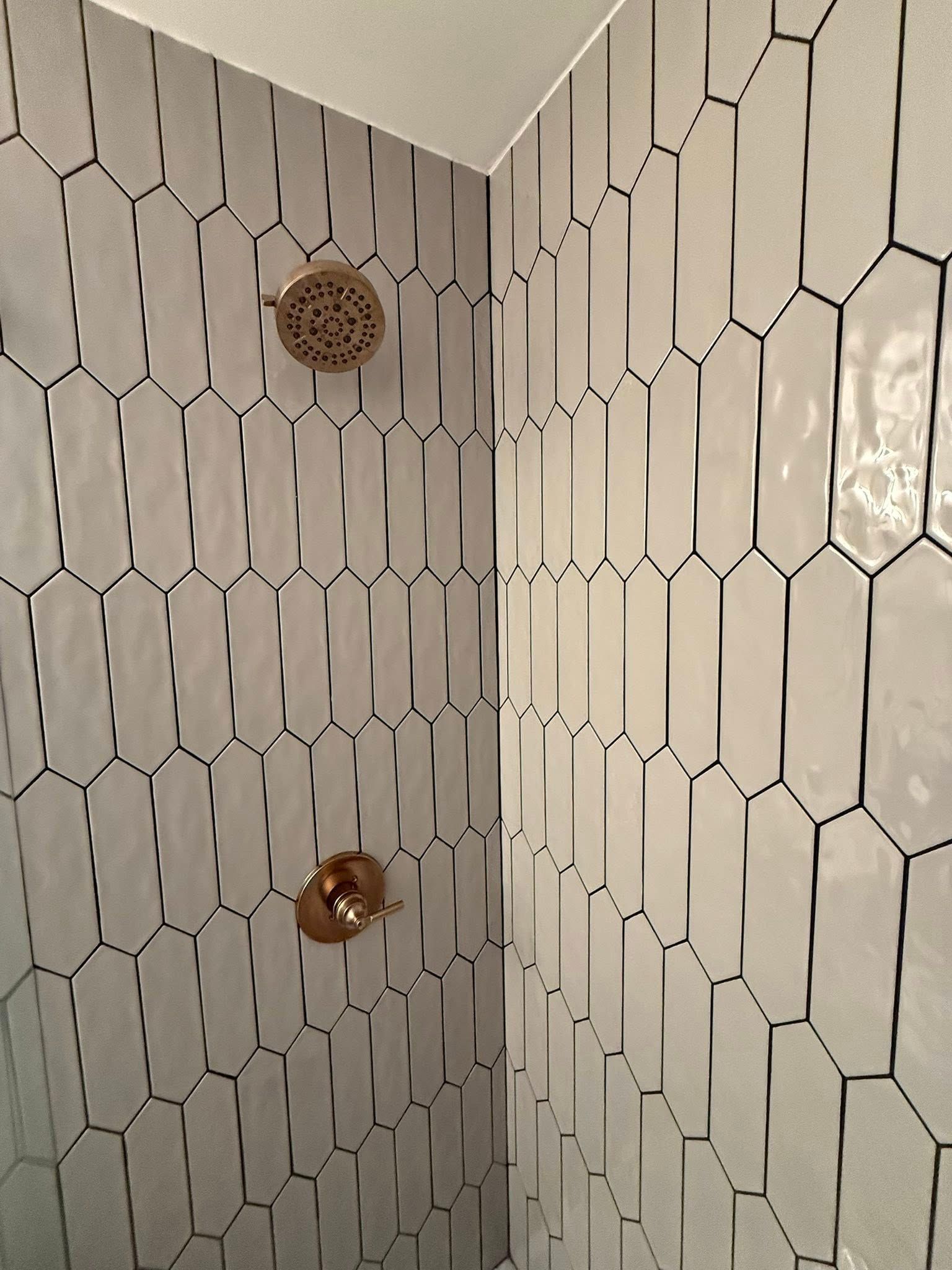 Shower stall with white, elongated hexagon tiles and bronze fixtures.