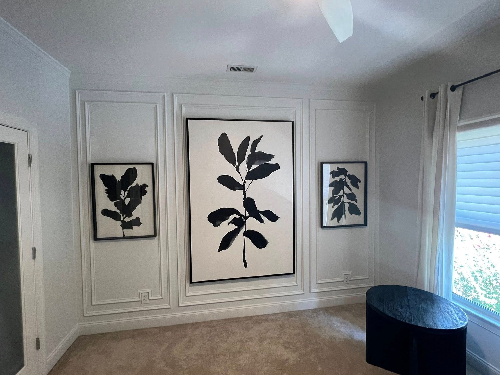 Room with white walls, three black-and-white botanical prints, and a black oval table.