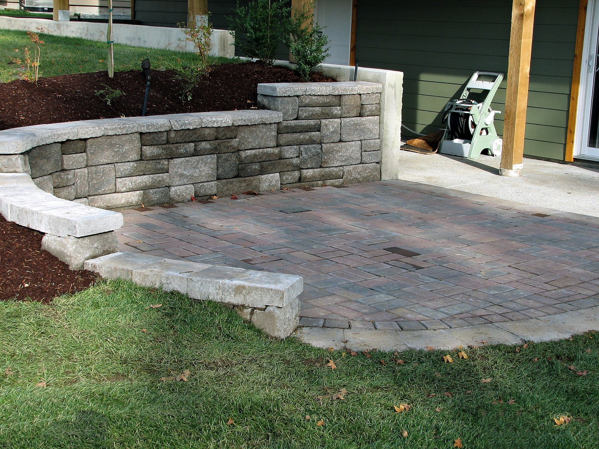 Stone patio with retaining wall and green grass.