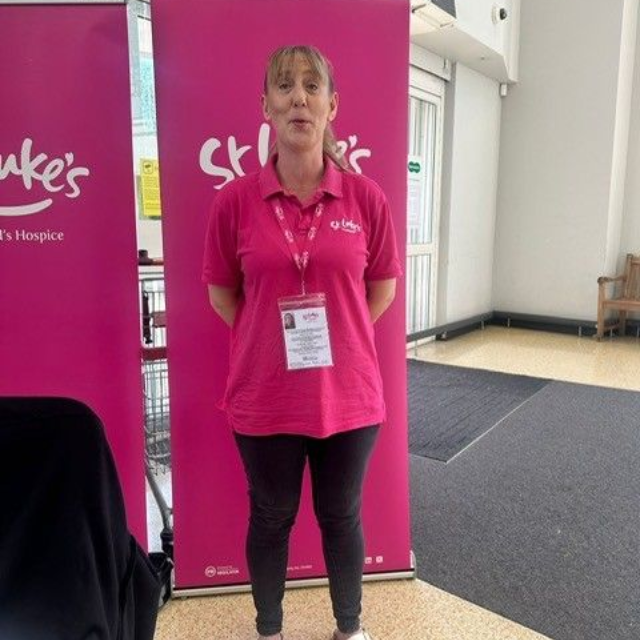Woman in pink polo shirt and black leggings, in front of a St. Luke's Hospice banner.