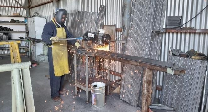 Persona con equipo de protección moliendo una barra de metal en el taller, saltando chispas.