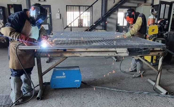 Dos soldadores trabajan en una estructura metálica, saltando chispas. Llevan equipo de protección en un taller.