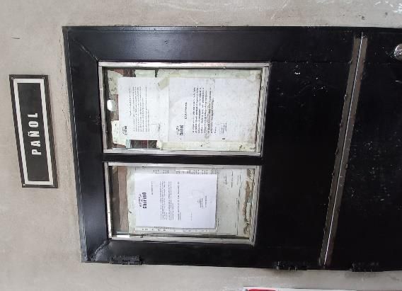 Panel negro con dos porta documentos que contienen papeles blancos, junto a un cartel de “PAROL” en una pared de color claro.