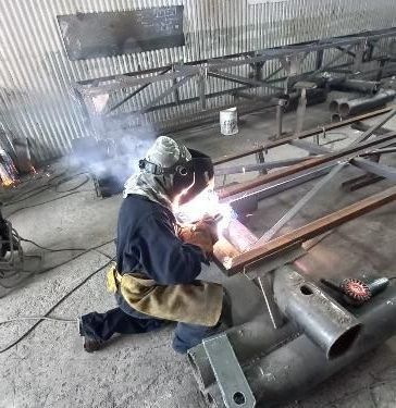 Soldador en taller soldando estructura metálica; chispas brillantes.