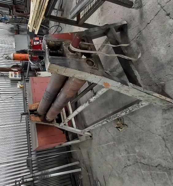 Máquina de rodillos metálicos en un taller. Estructura metálica gris, cuerpo de la máquina rojo y gris, tres rodillos.