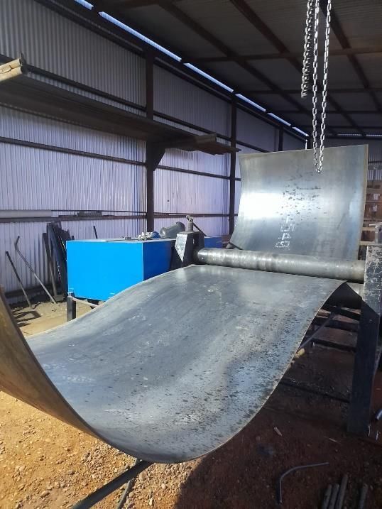 Una máquina lamina una chapa metálica en forma curva en un taller.