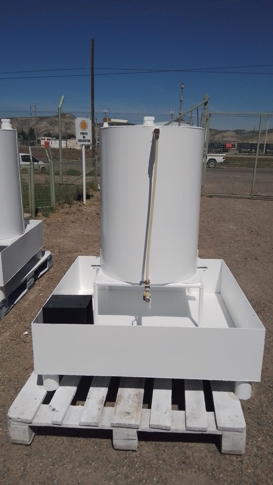 Tanque industrial blanco sobre una unidad de contención blanca, encima de un palé al aire libre.