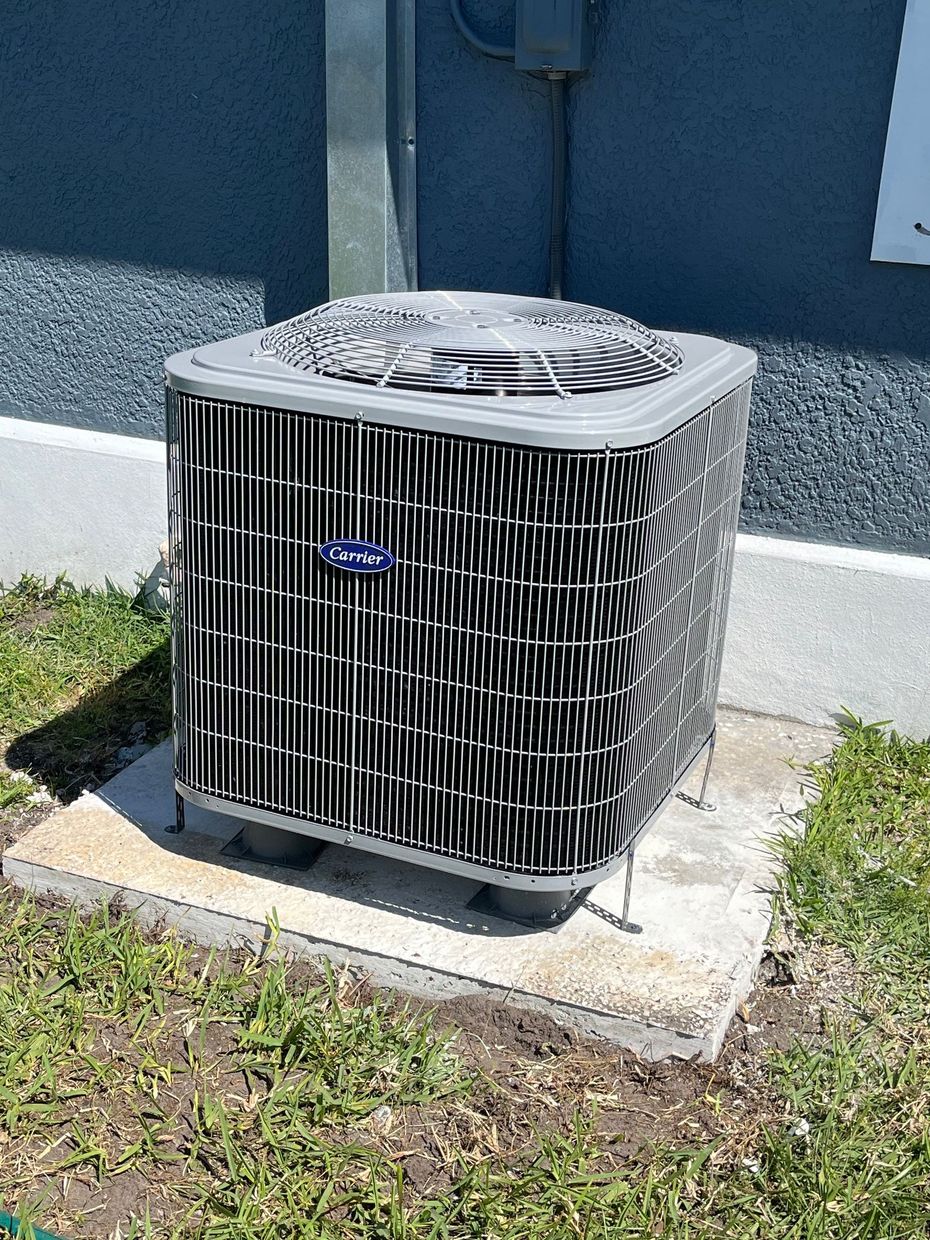 A large air conditioner is sitting on top of a concrete block in the grass.