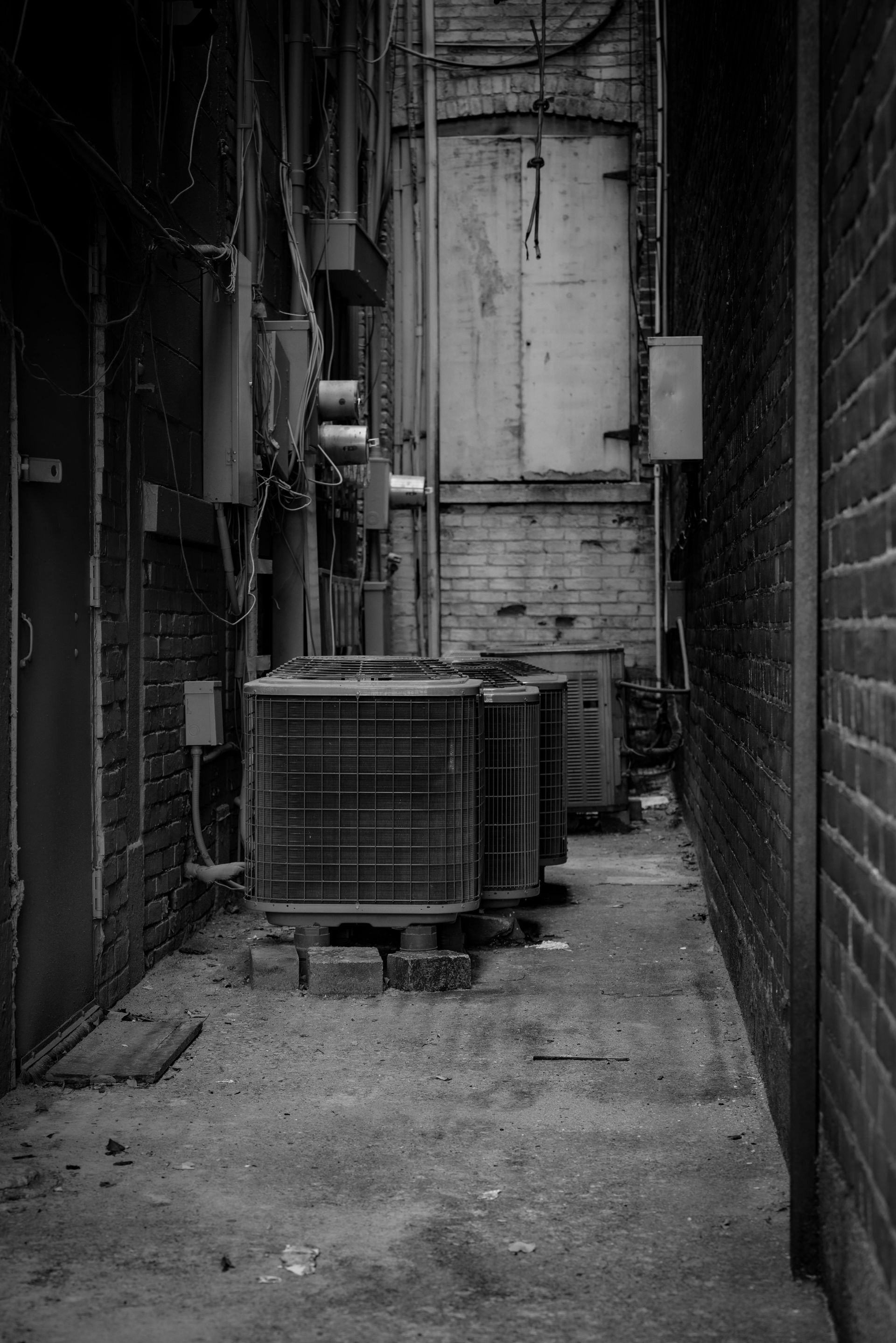 A black and white photo of an alleyway with a row of air conditioners.