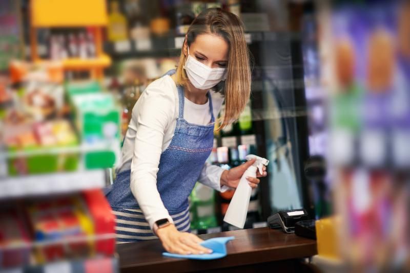 A woman wearing a mask is cleaning a counter in a store.
